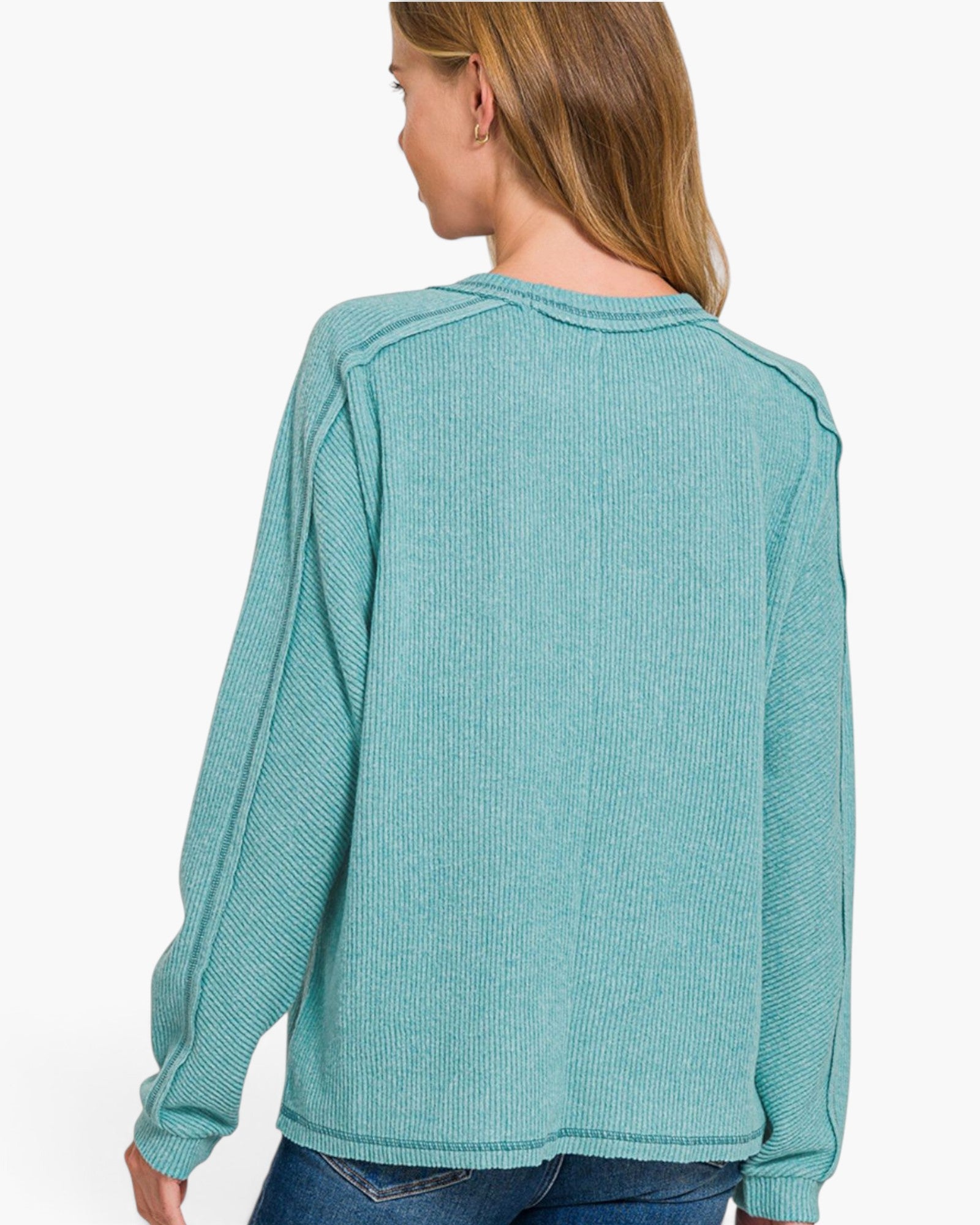 A woman shown from the back wearing a ribbed knit long-sleeve sweater in a muted teal green color, paired with blue jeans against a plain white background.