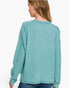 A woman shown from the back wearing a ribbed knit long-sleeve sweater in a muted teal green color, paired with blue jeans against a plain white background.