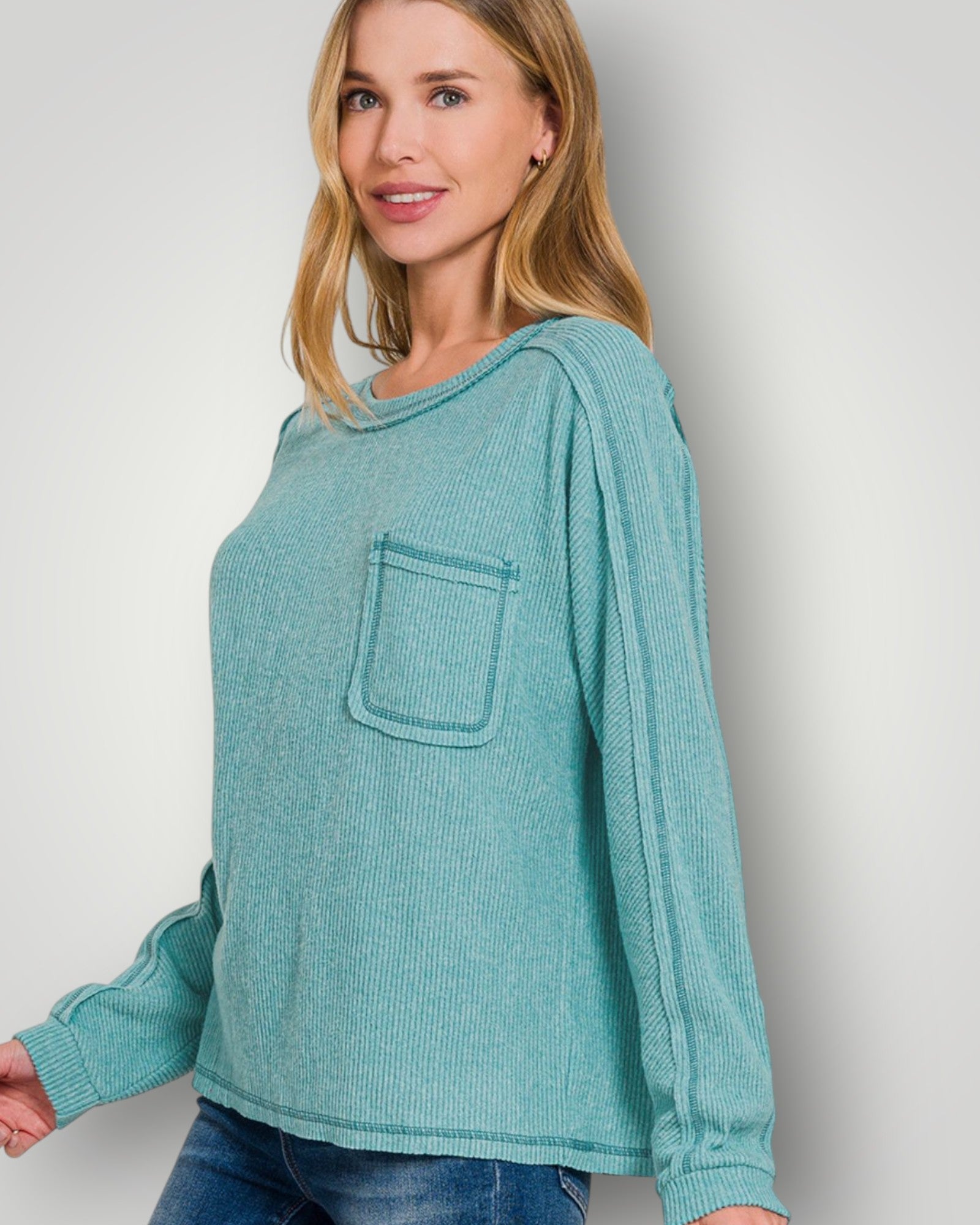Woman wearing a teal long-sleeve top with a pocket against a plain background