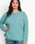 A woman wearing a ribbed knit long-sleeve top in a muted teal green color, featuring a chest pocket, paired with blue jeans against a plain white background.