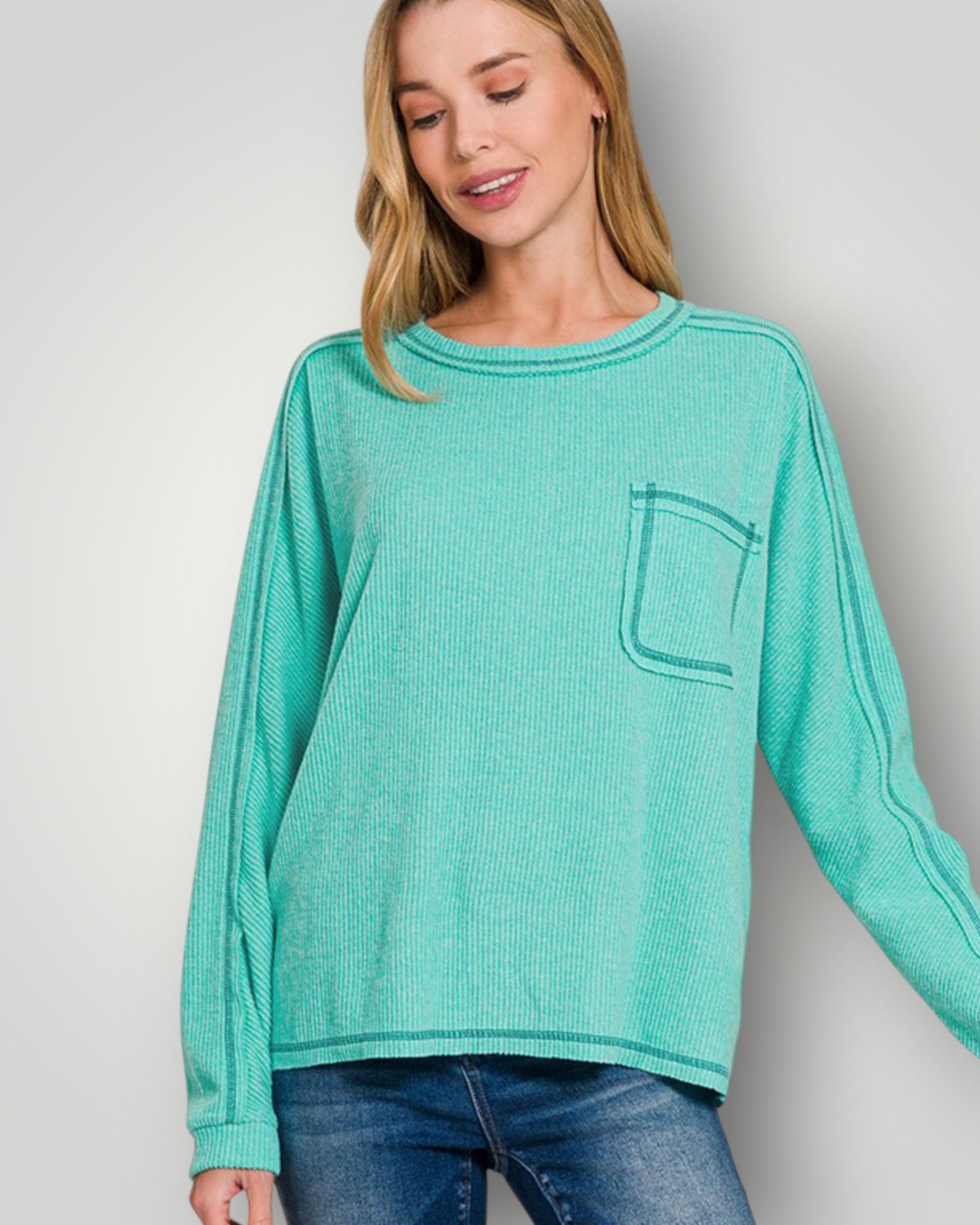 Woman wearing a teal long-sleeve top with a pocket on a plain background