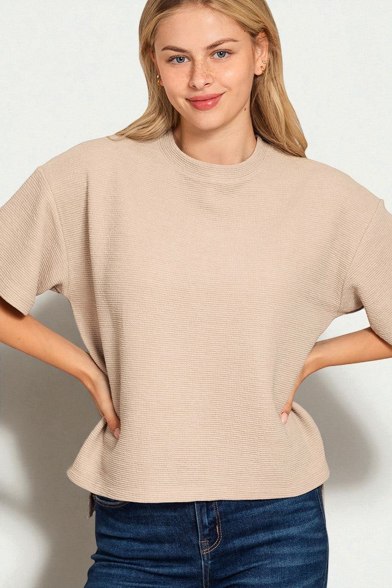 Woman wearing a beige sweater and blue jeans against a plain background