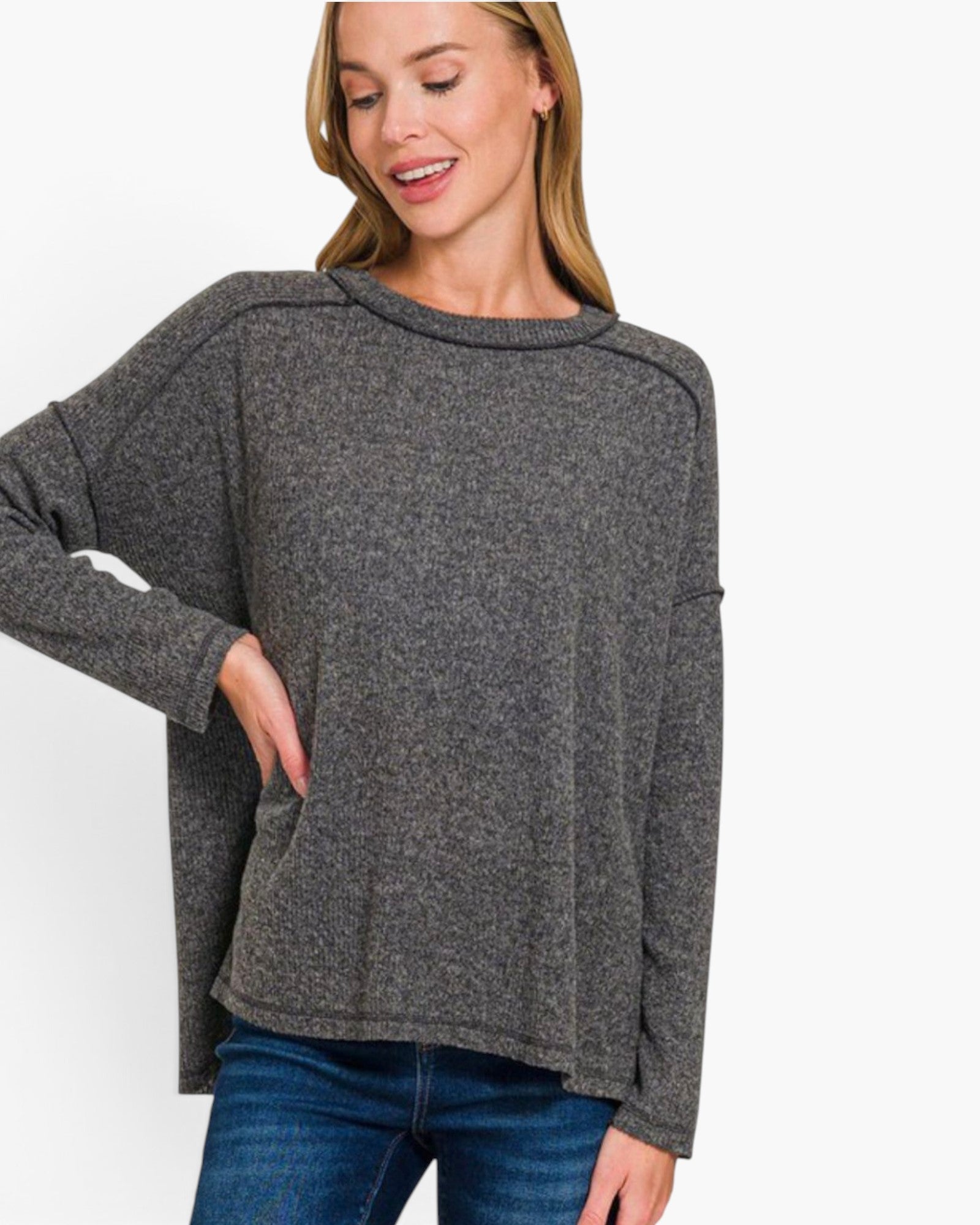 A woman wearing a dark gray heathered knit sweater with a crew neck and drop shoulders, paired with blue jeans, against a plain white background.