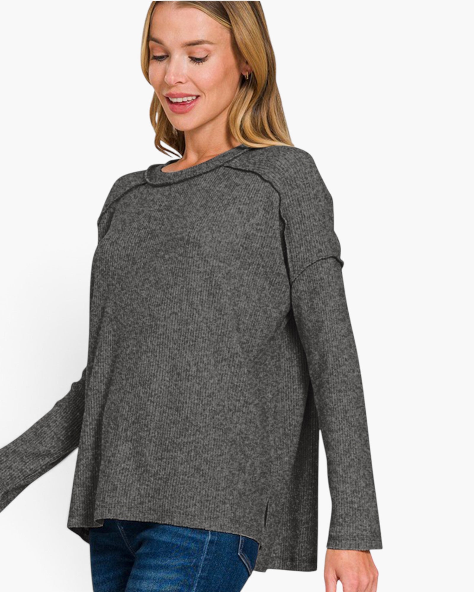 A woman wearing a dark gray knit sweater with a wide draped neckline and long sleeves, paired with blue jeans, against a plain white background.