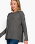 A woman wearing a dark gray knit sweater with a wide draped neckline and long sleeves, paired with blue jeans, against a plain white background.