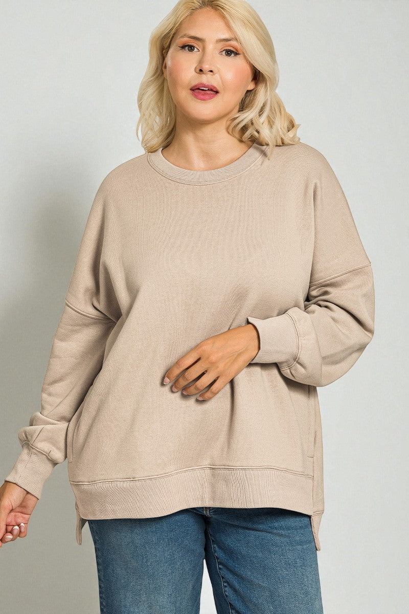 Woman wearing a beige sweater and blue jeans against a plain background