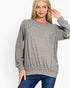 A woman wearing a heather gray long-sleeve crewneck sweater and blue jeans, posing against a solid white studio background.