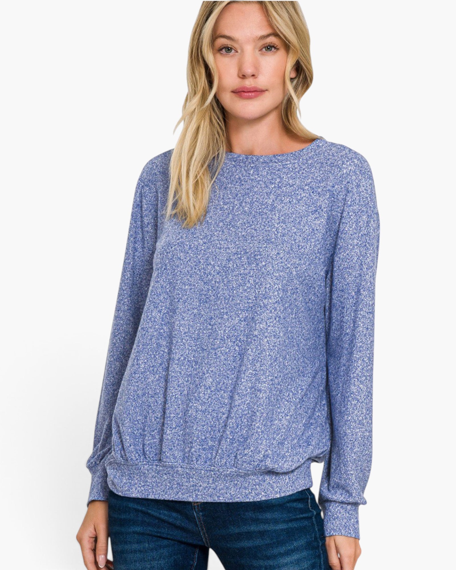 A woman wearing a long-sleeve crewneck sweater in a heathered periwinkle blue color, paired with dark blue jeans, against a plain white background.