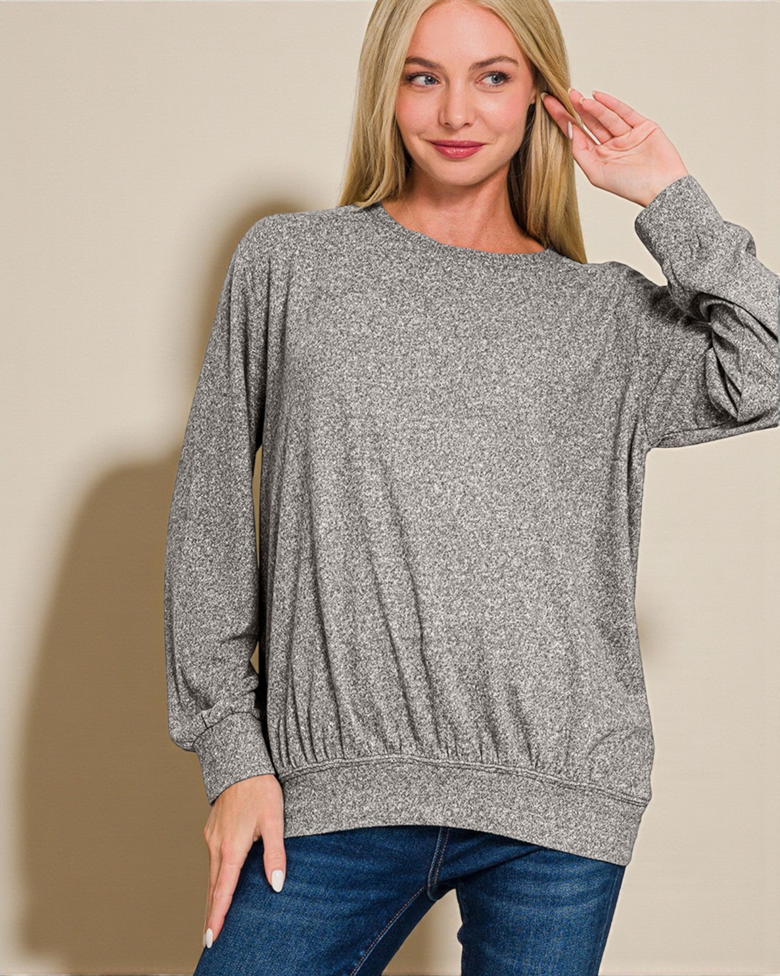 Woman wearing a gray sweater and blue jeans against a beige background