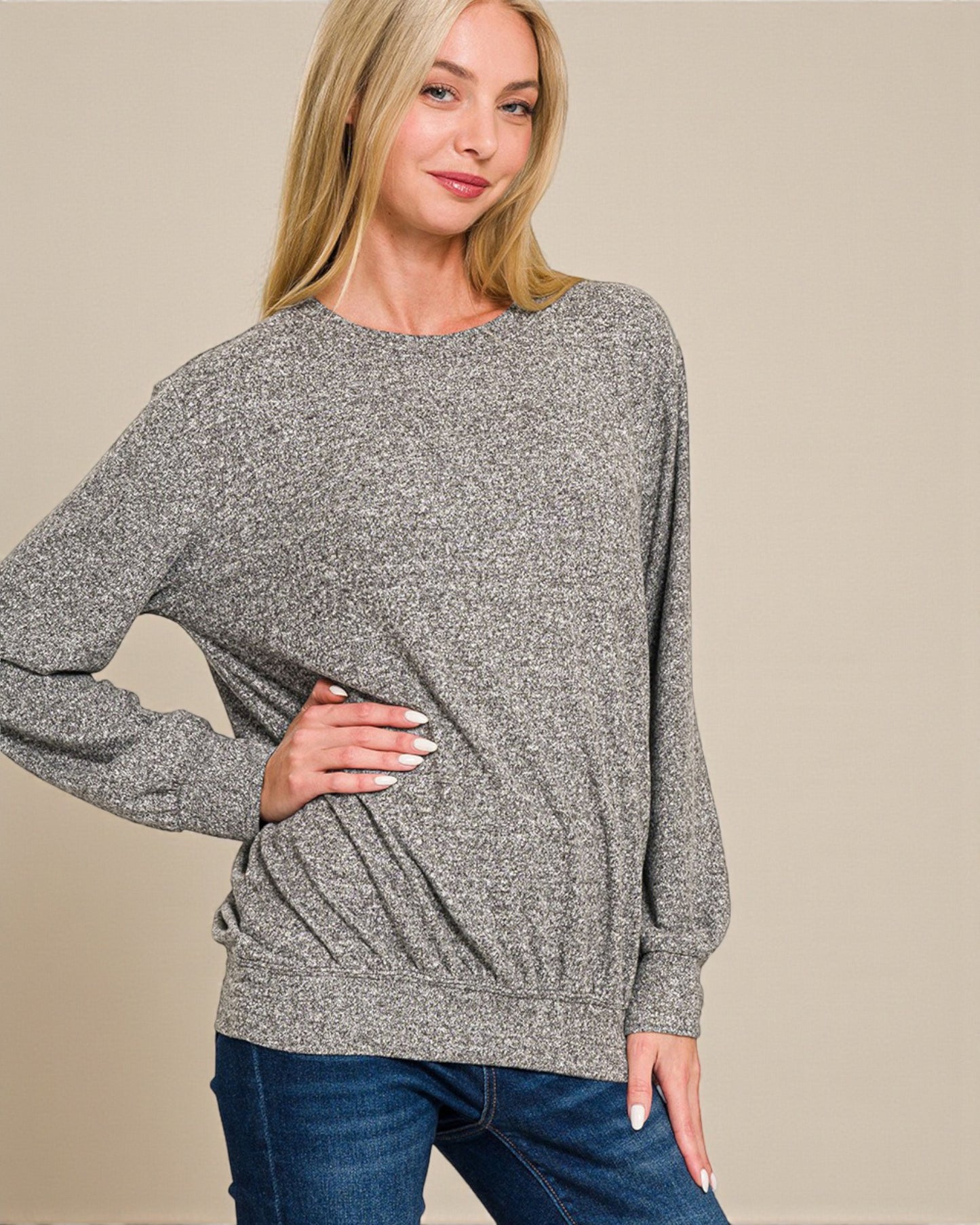 Woman wearing a gray sweater and blue jeans against a beige background