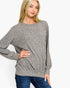 A woman wearing a heather gray long-sleeve crewneck sweater and blue jeans, posing against a solid white studio background.