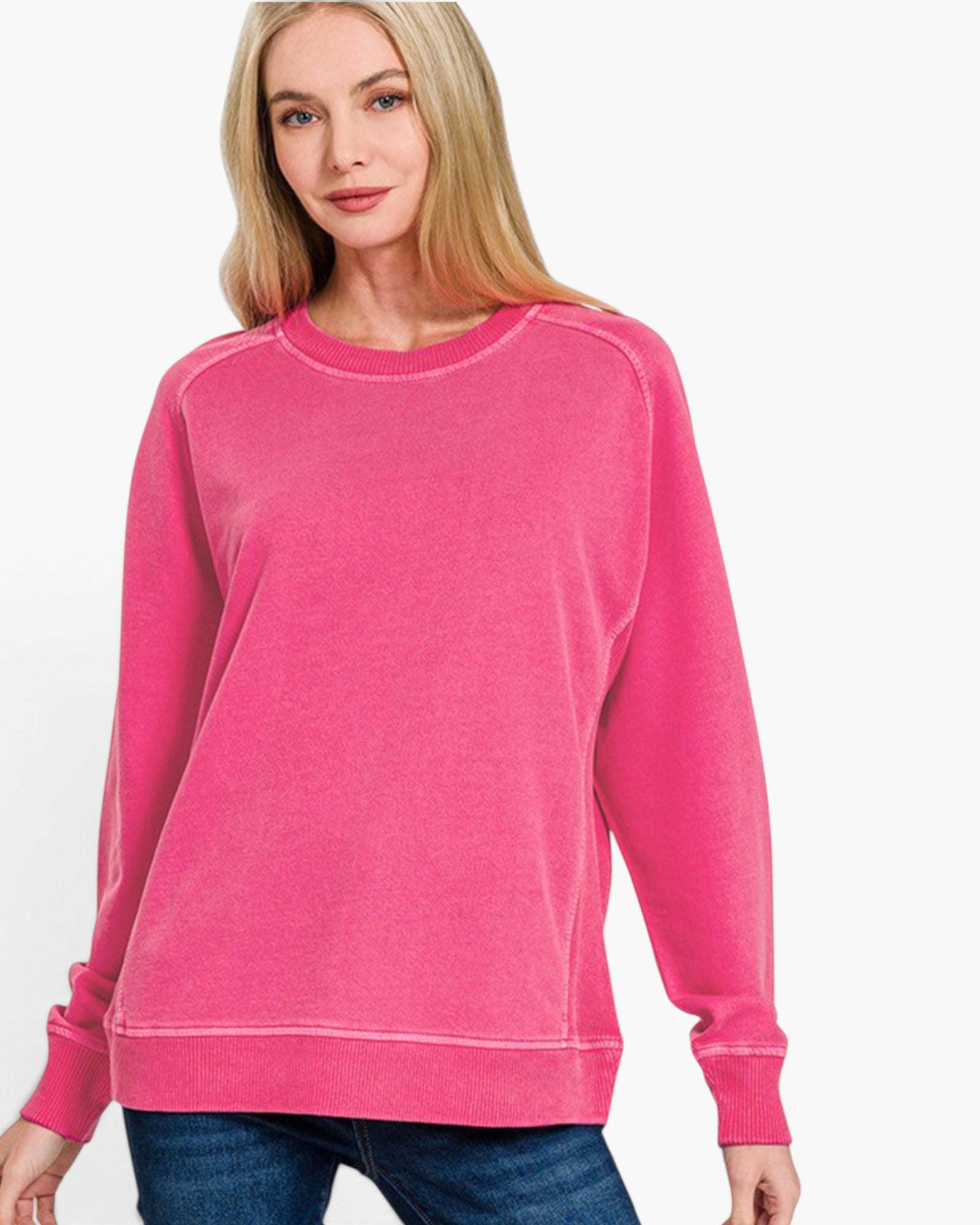 A woman wearing a bright pink crewneck sweatshirt with raglan sleeves, paired with blue jeans, against a plain white background.