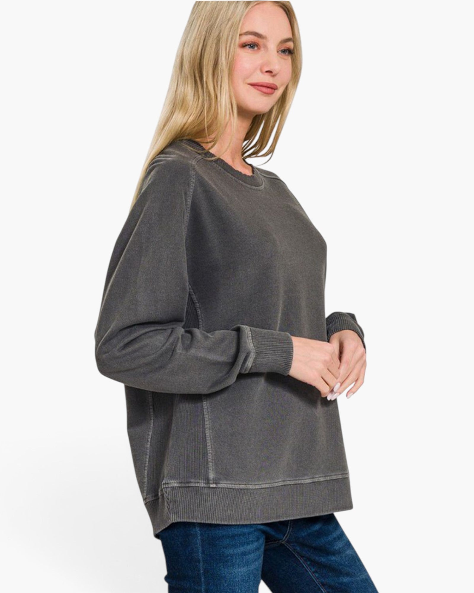 A woman wearing a dark gray washed long-sleeve sweatshirt and blue jeans, shown from a side profile against a plain white background.