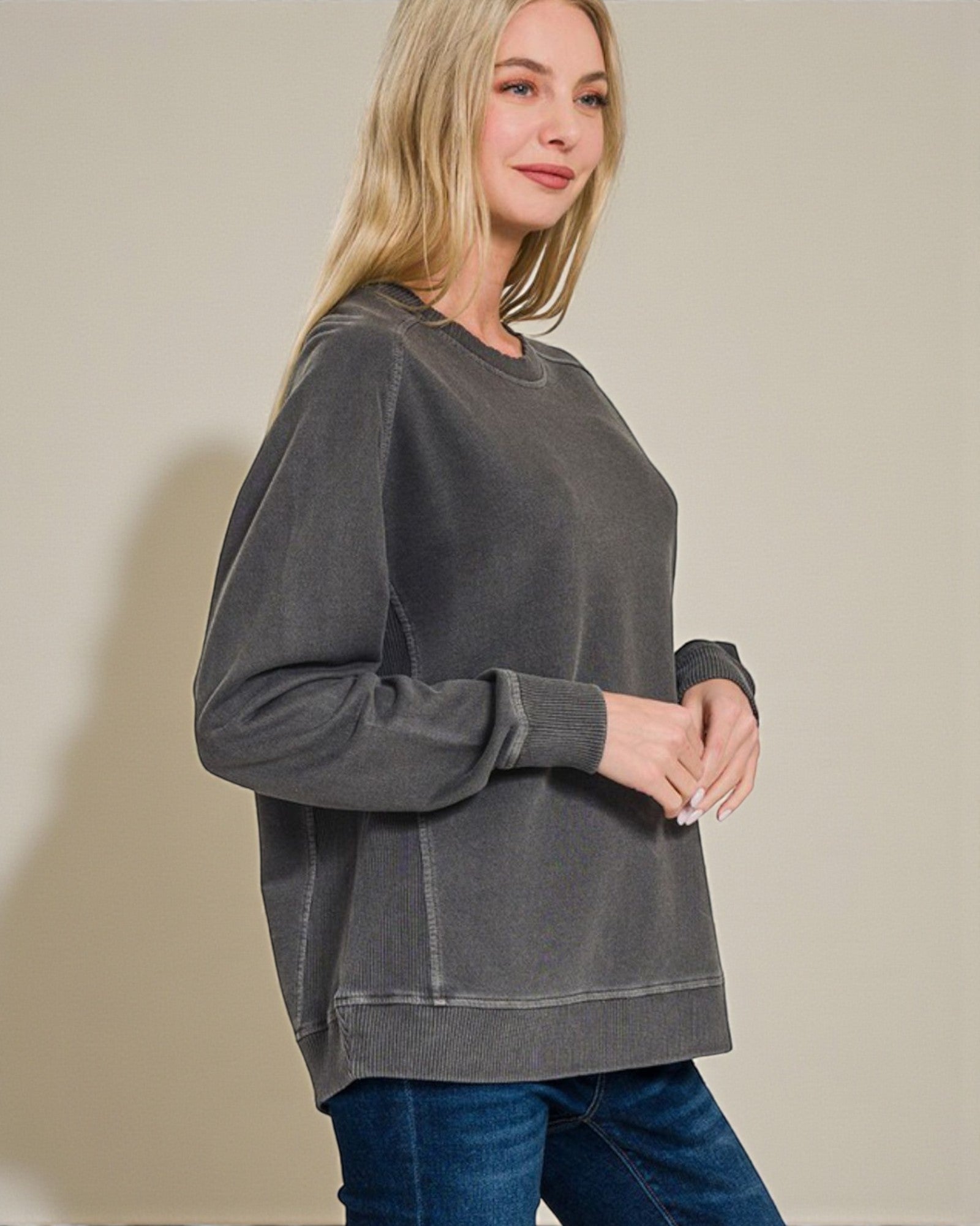 Woman wearing a gray sweatshirt and blue jeans against a beige background