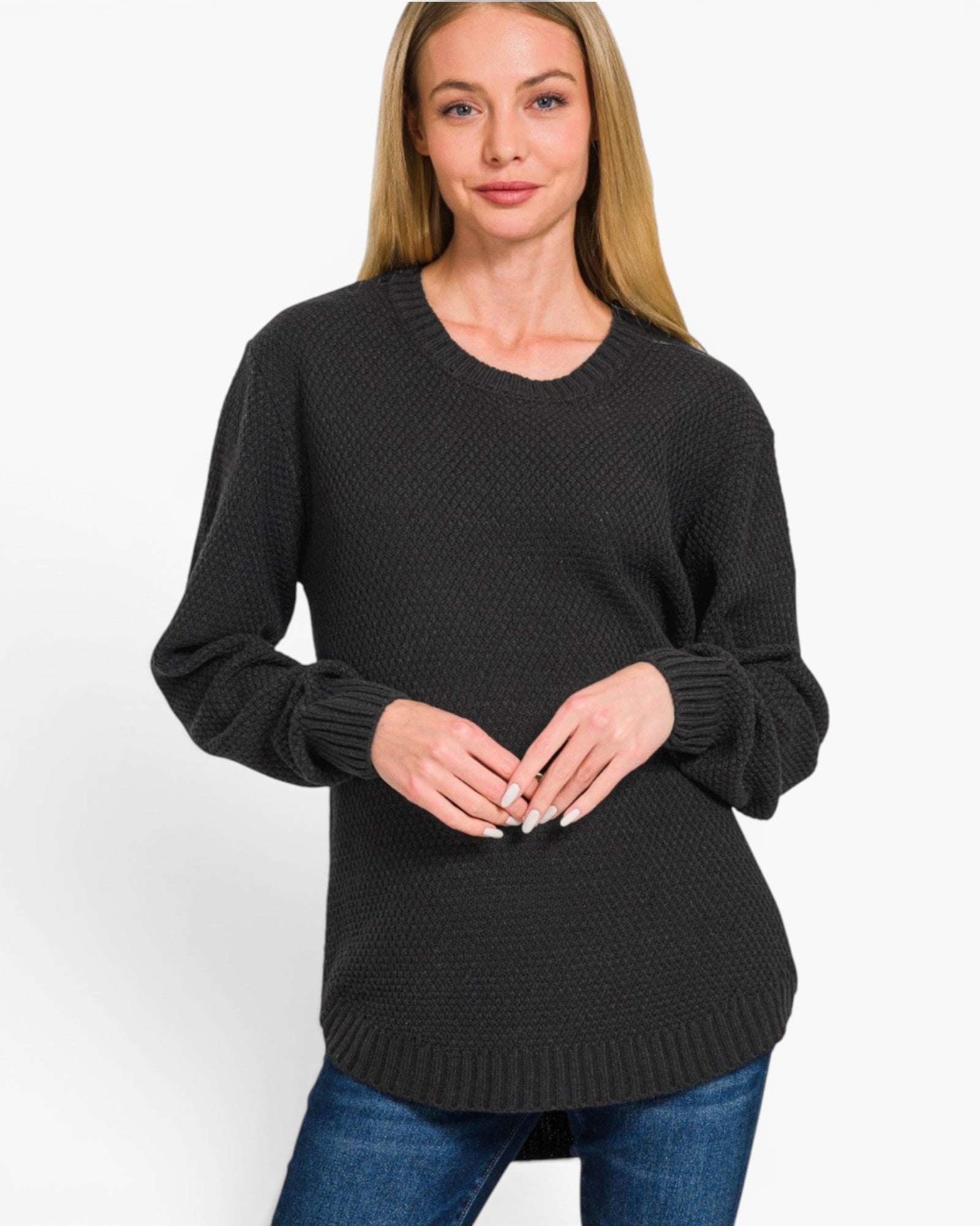 A woman wearing a black textured knit crewneck sweater with long sleeves and ribbed cuffs, paired with blue jeans, against a plain white background.