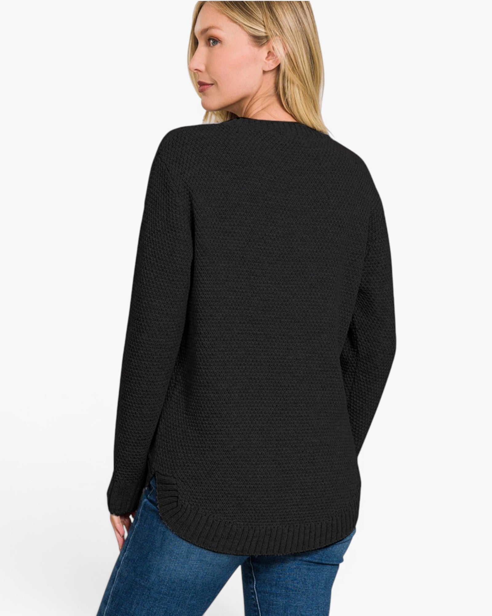 A woman wearing a black textured knit sweater and blue jeans, shown from a back-three-quarter view against a plain white studio background.