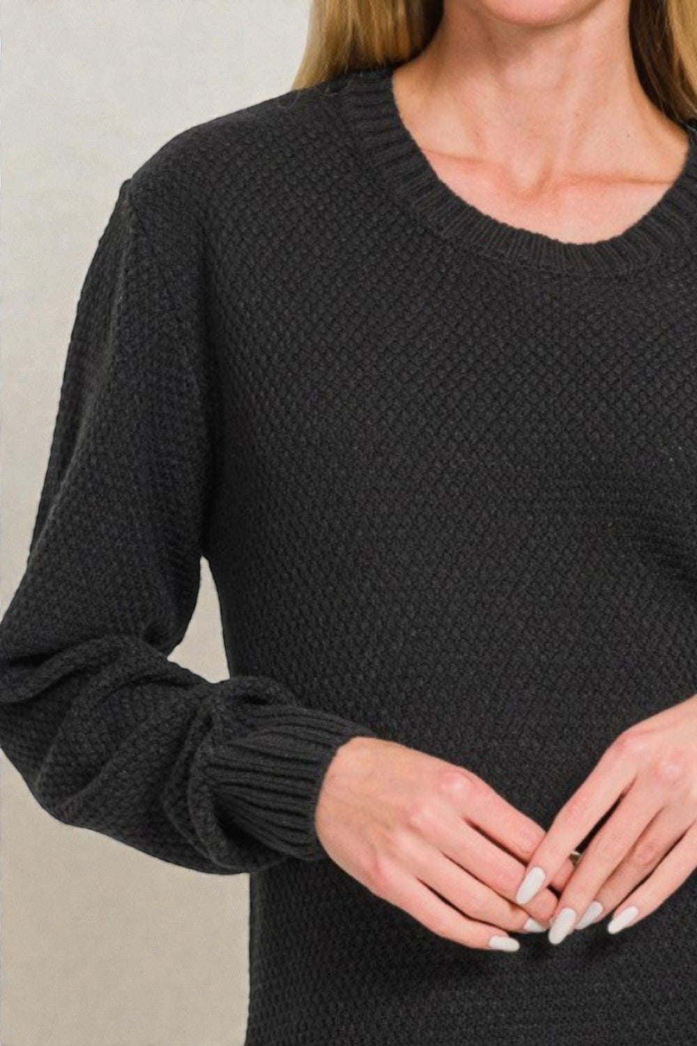 Black textured sweater worn by a person against a neutral background
