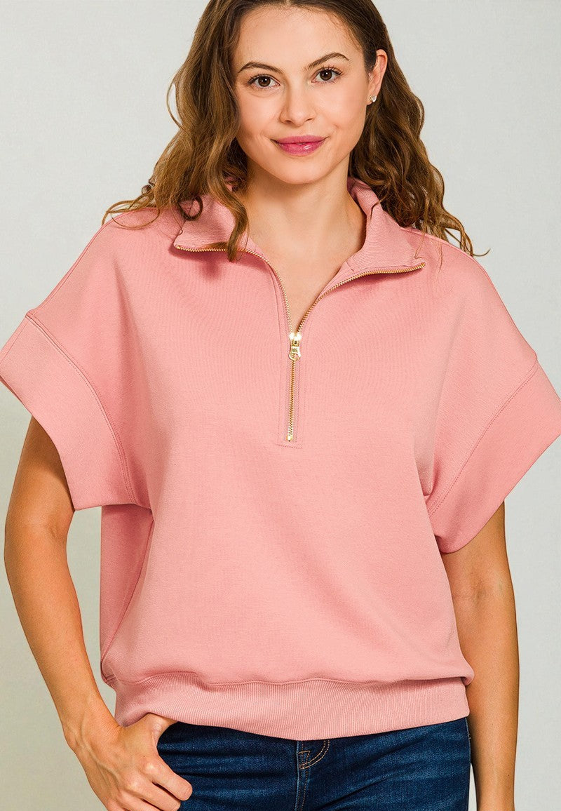 Woman wearing a pink short-sleeve top with a zipper on a plain background