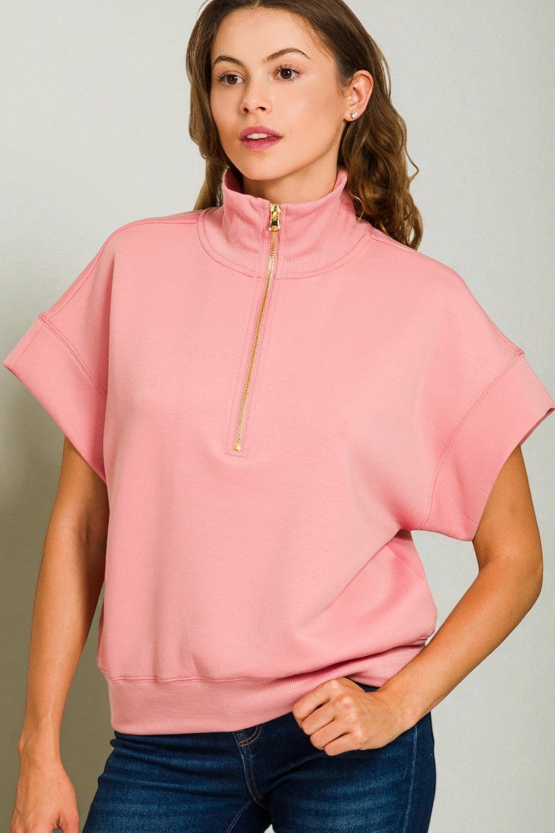 Woman wearing a pink short-sleeve top with a gold zipper on a plain background