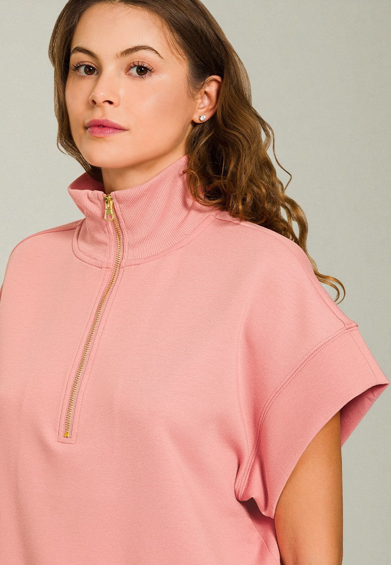 Woman wearing a pink short-sleeve top with a zipper on a plain background