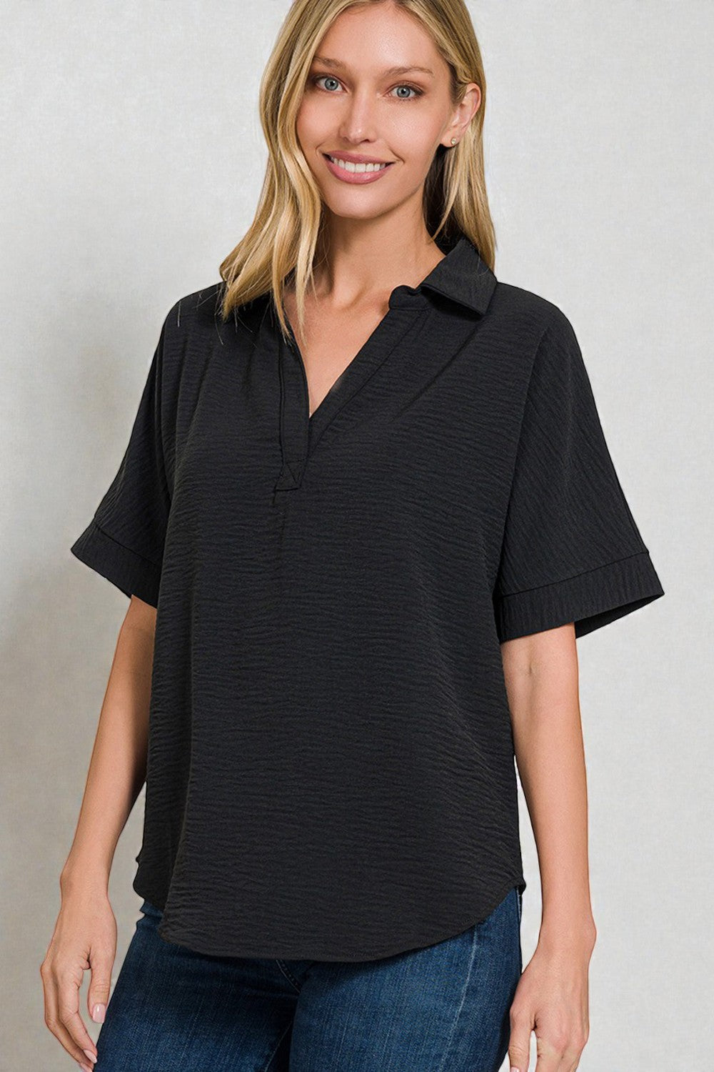 Woman wearing a black short-sleeve shirt with a collar against a plain background