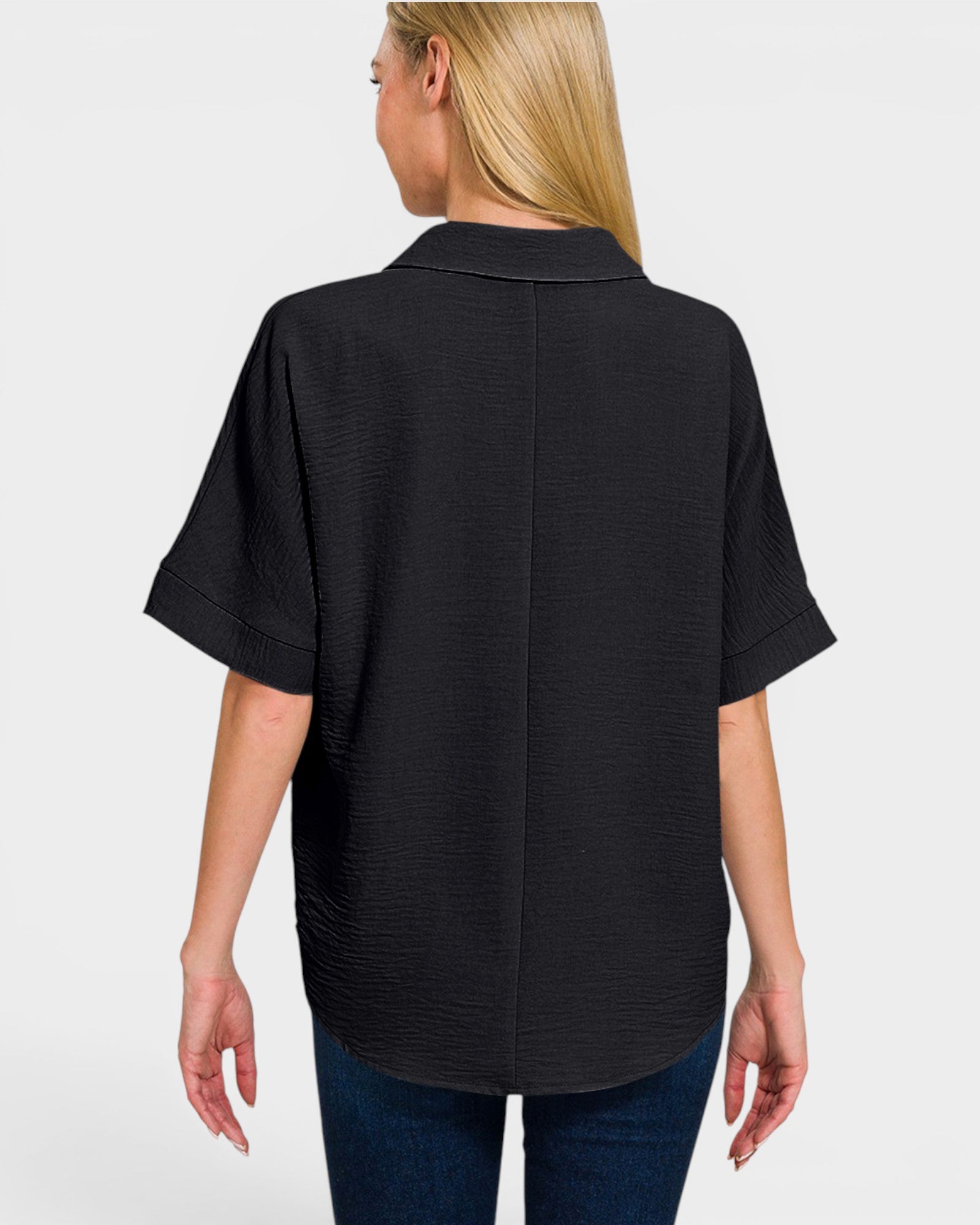 A woman shown from the back wearing a black short-sleeve textured collared blouse with rolled cuffs, paired with blue jeans, against a light gray studio background.