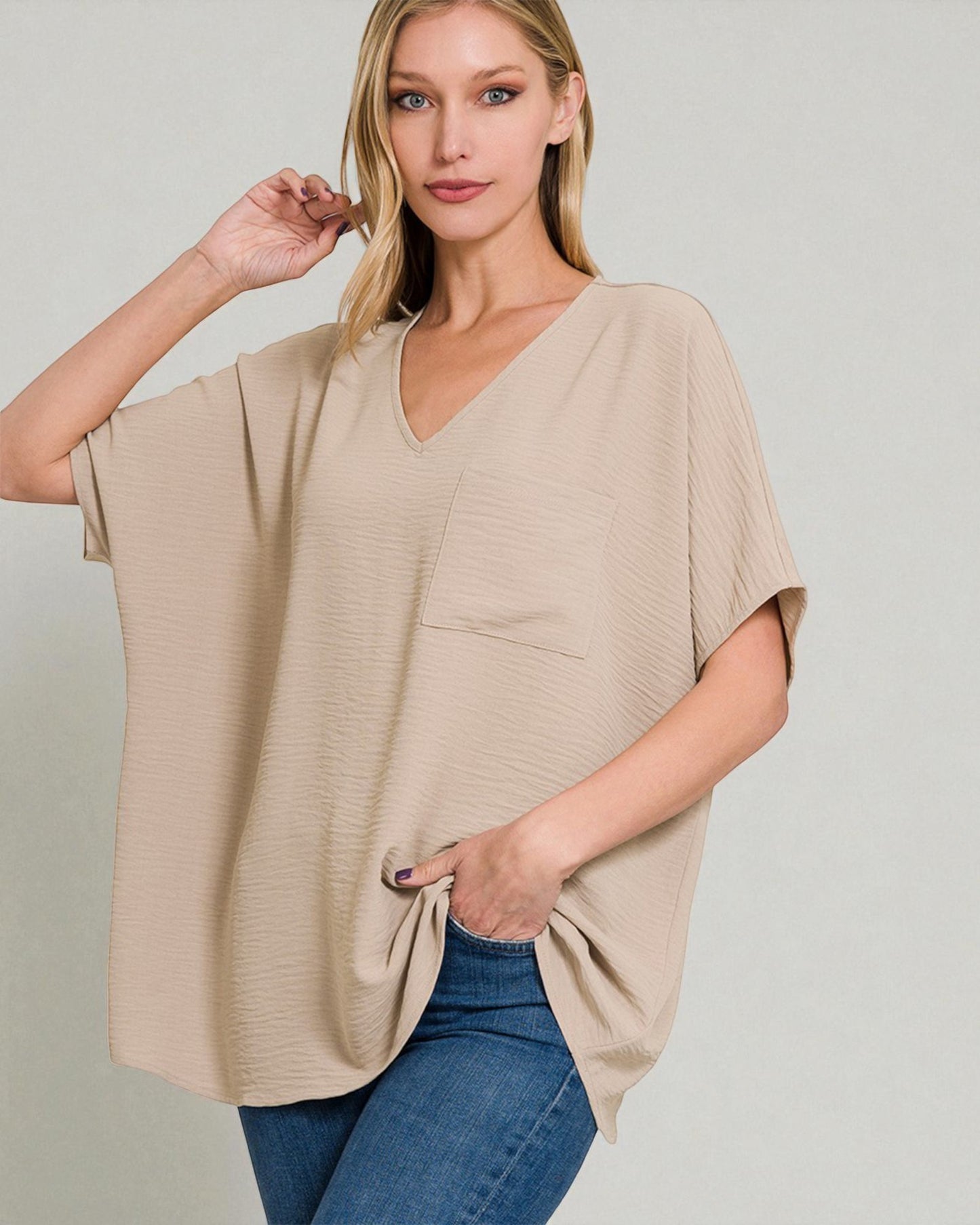 Woman wearing a beige poncho over a blue top against a plain background