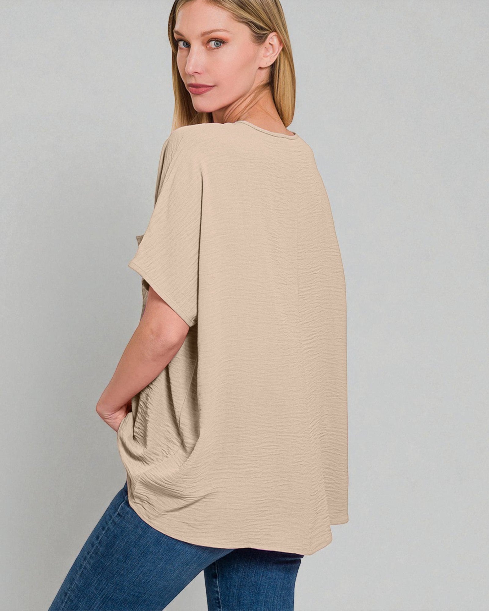 Woman wearing a beige poncho over a blue outfit on a gray background