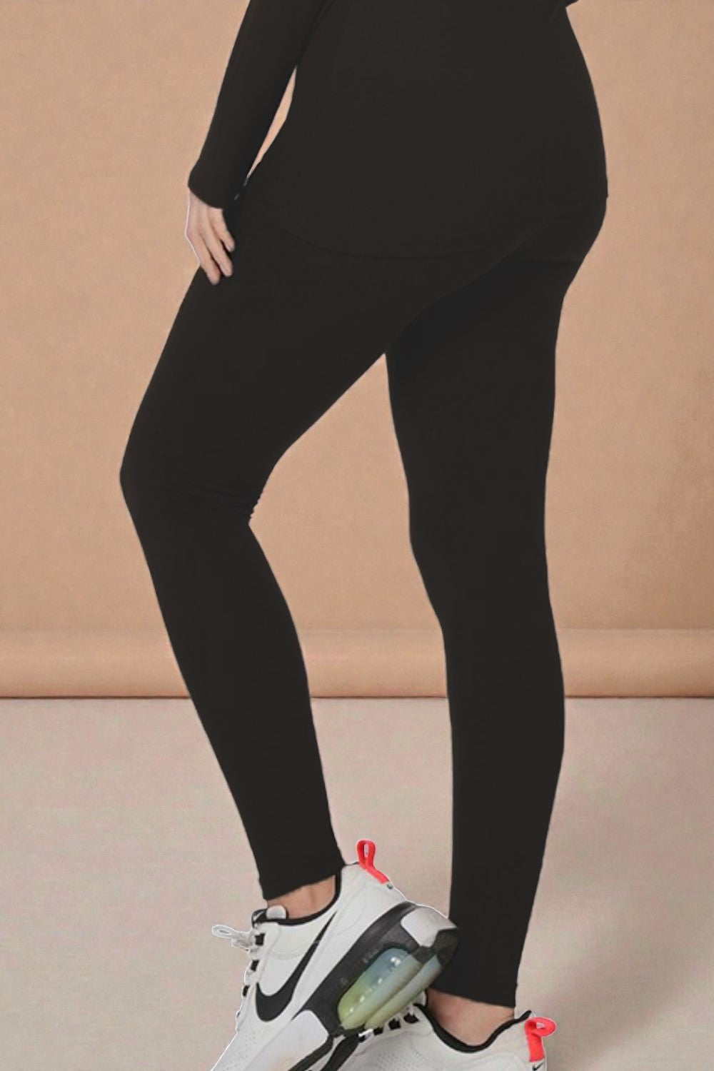 Person wearing black leggings and white sneakers on a beige background
