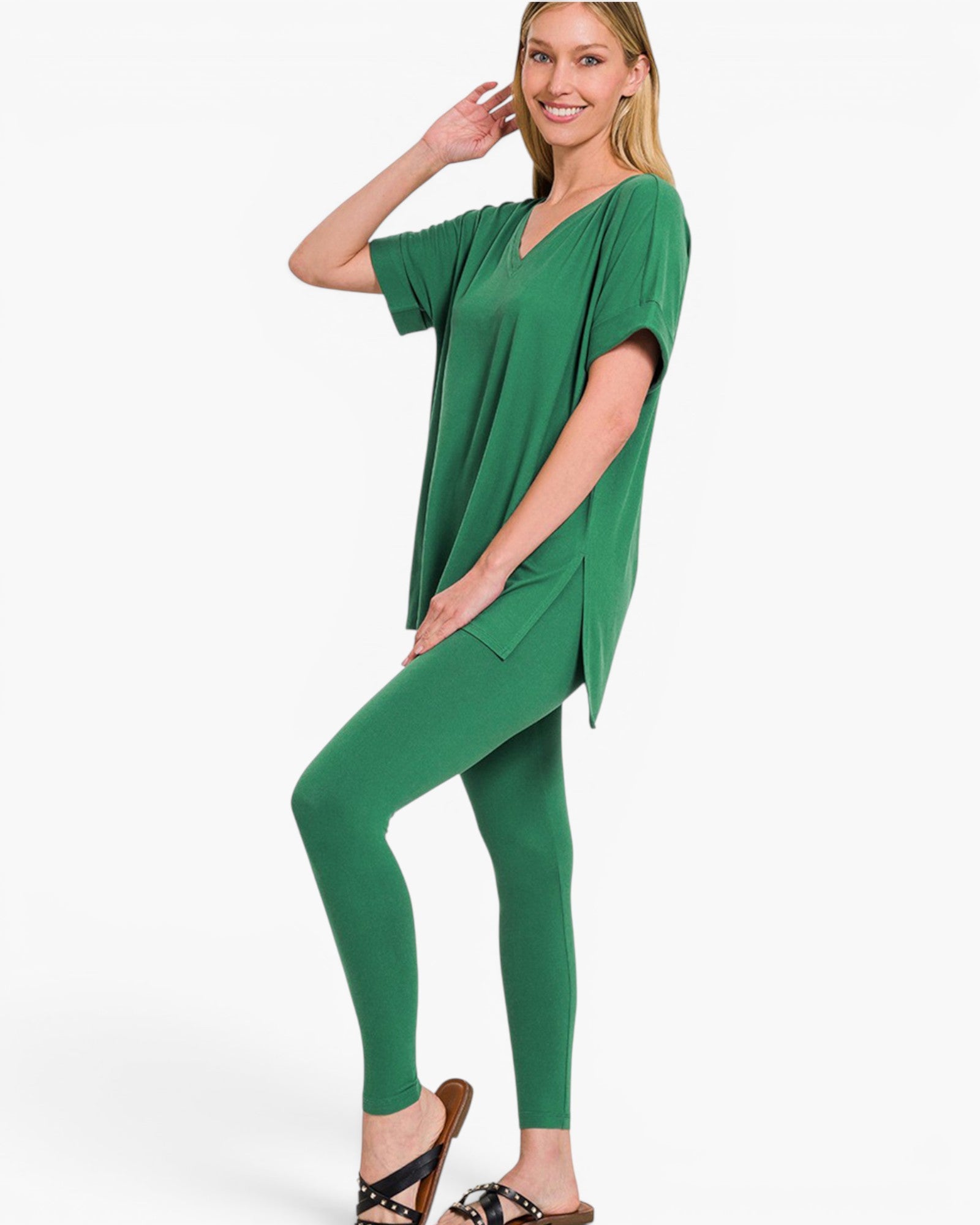 A woman modeling a matching green lounge set consisting of a short-sleeve V-neck top and high-waisted leggings, paired with brown sandals, against a plain white studio background.