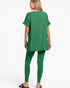 A woman shown from the back wearing a matching green short-sleeve tunic top and leggings set, paired with dark brown sandals, against a plain white studio background.