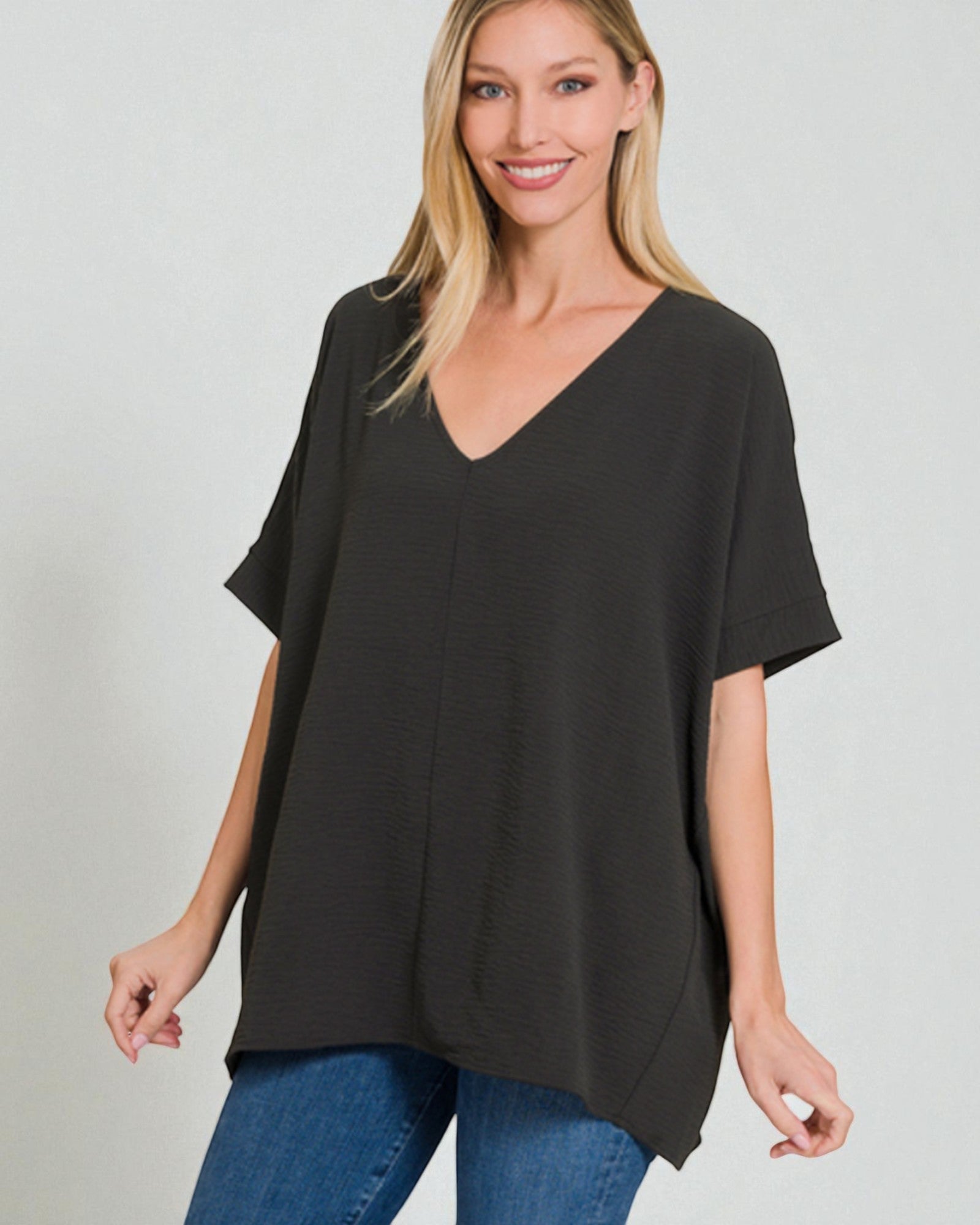 Woman wearing a black oversized t-shirt and blue jeans on a light gray background