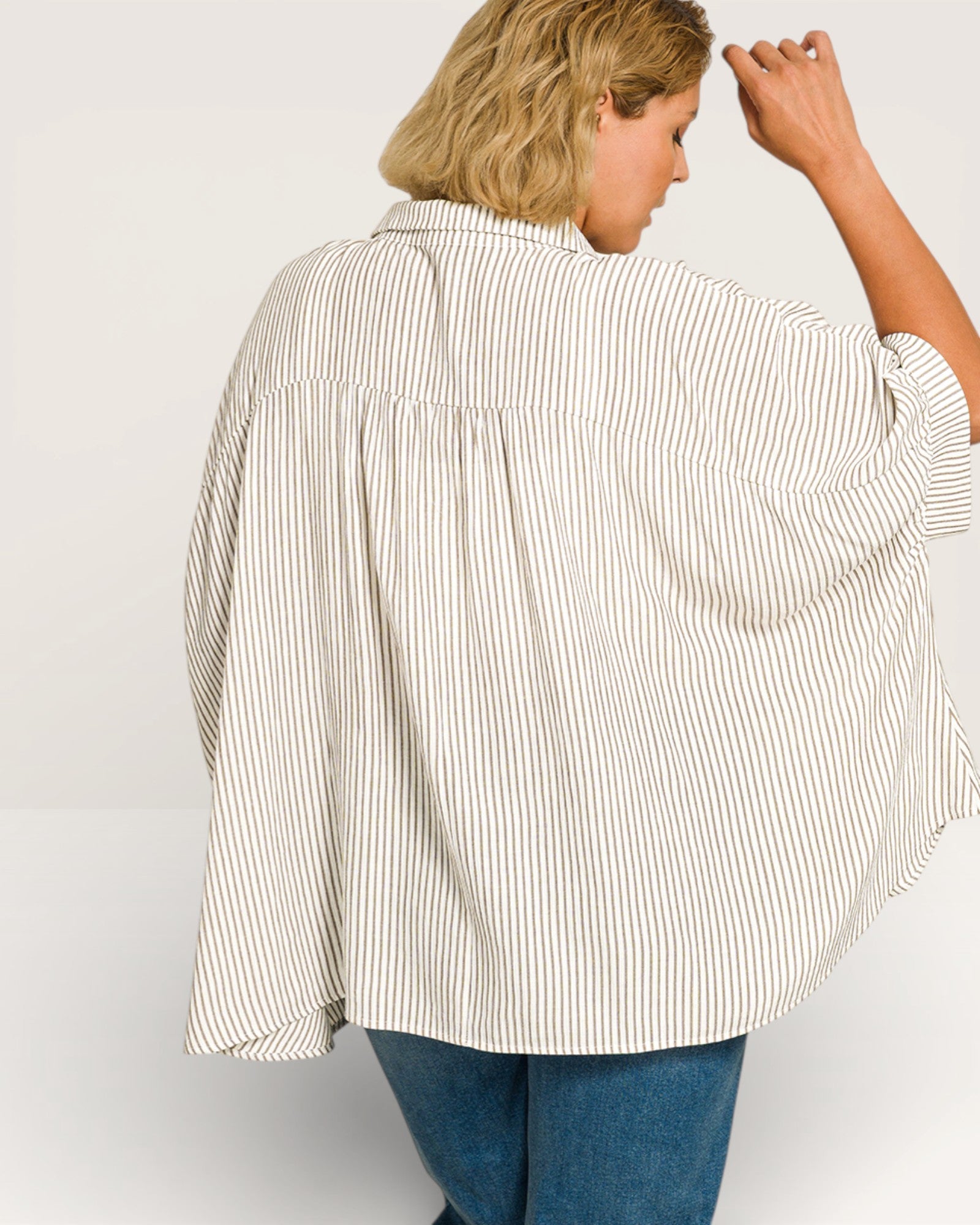 Person wearing a white and gray striped shirt with blue jeans on a plain background