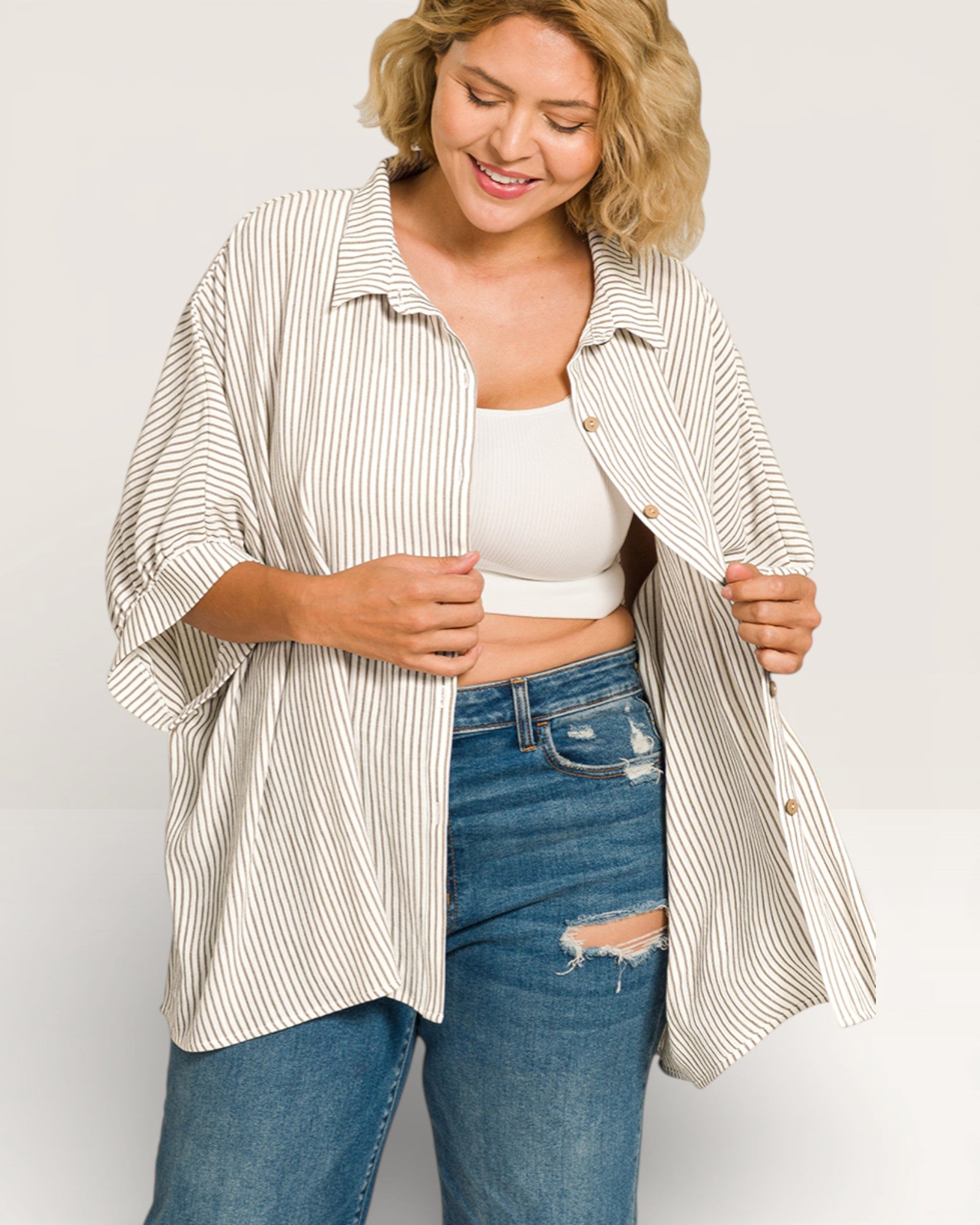 Woman wearing a striped shirt over a white top and blue jeans on a plain background