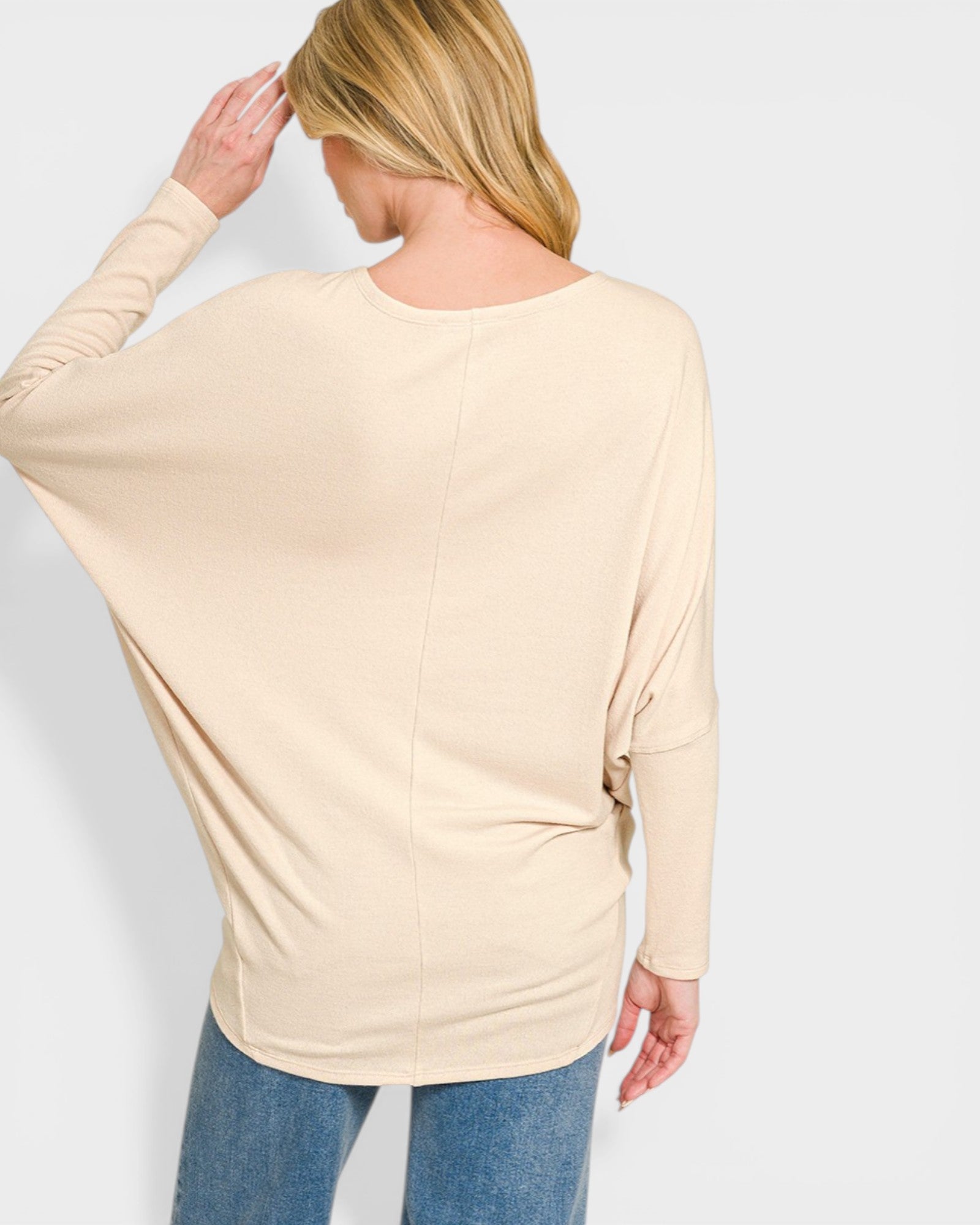 Woman wearing a beige long-sleeve top and blue jeans on a white background