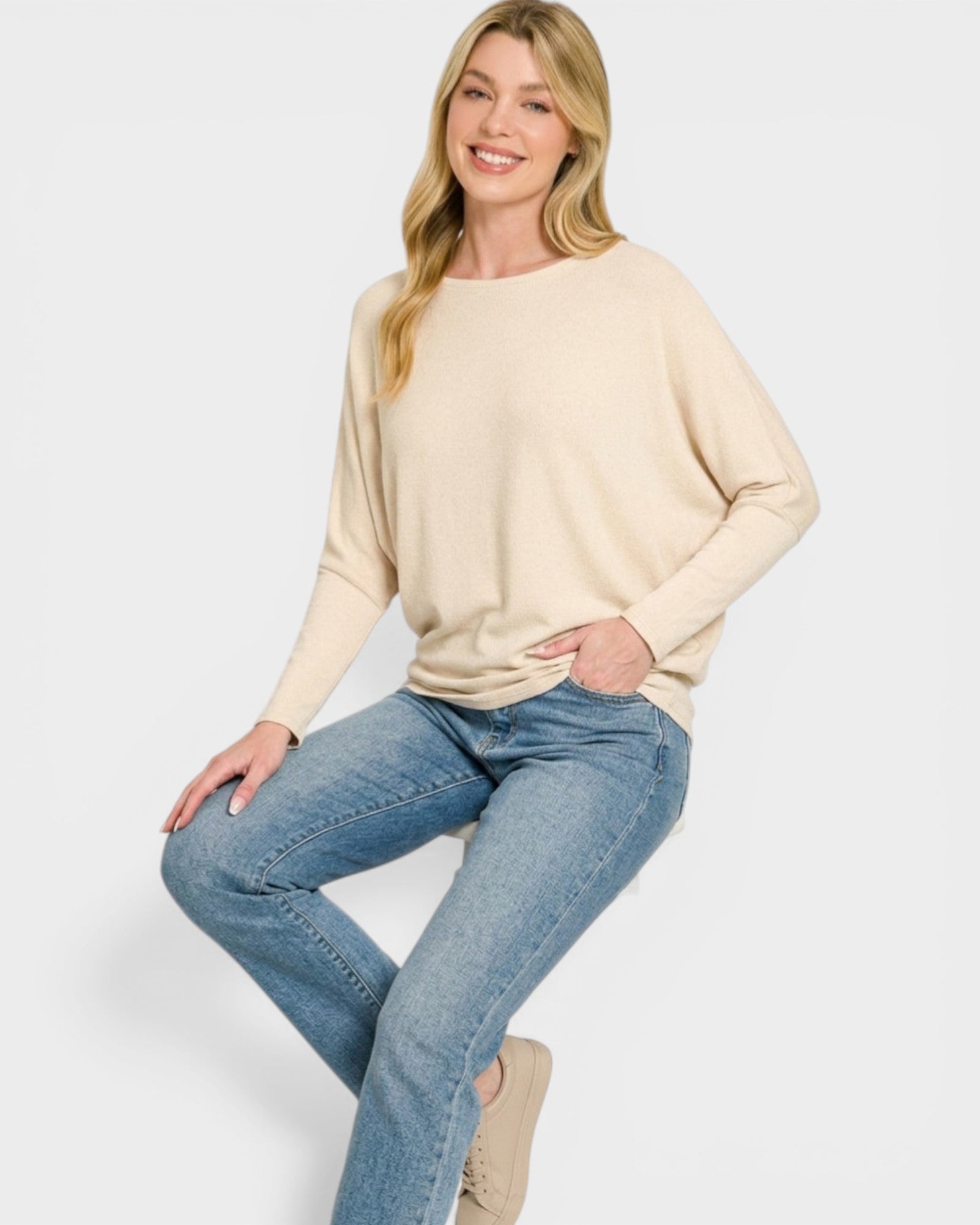 Woman wearing a beige sweater and blue jeans on a white background