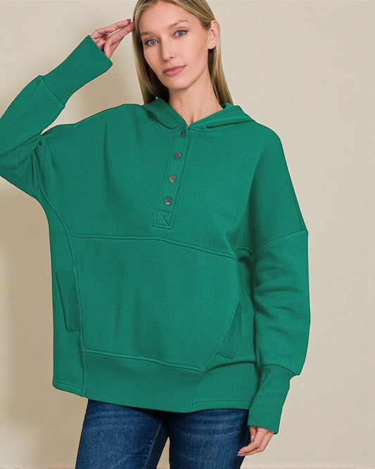 Person wearing a green hoodie with button details on a beige background
