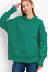 A woman wearing a bright green pullover hoodie with a buttoned henley-style neckline and a front kangaroo pocket, paired with blue jeans, against a plain light background.