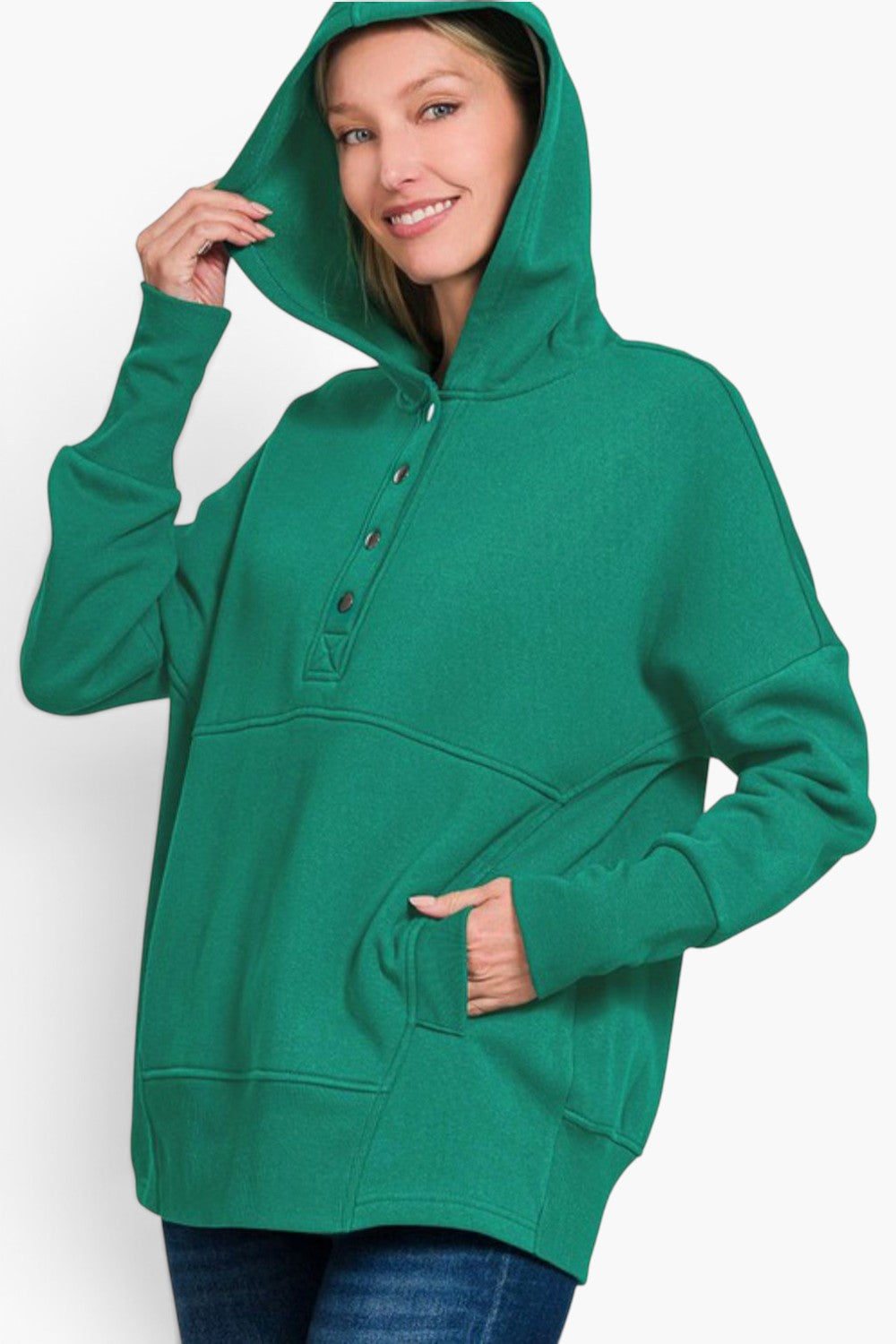 A woman wearing a bright green pullover hoodie with a buttoned henley neckline, front pockets, and a relaxed fit, paired with blue jeans against a plain light background.