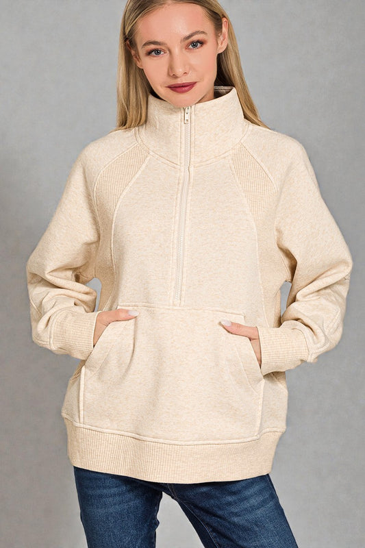 Woman wearing a beige zip-up hoodie against a gray background
