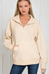 Woman wearing a beige zip-up sweatshirt against a white wall