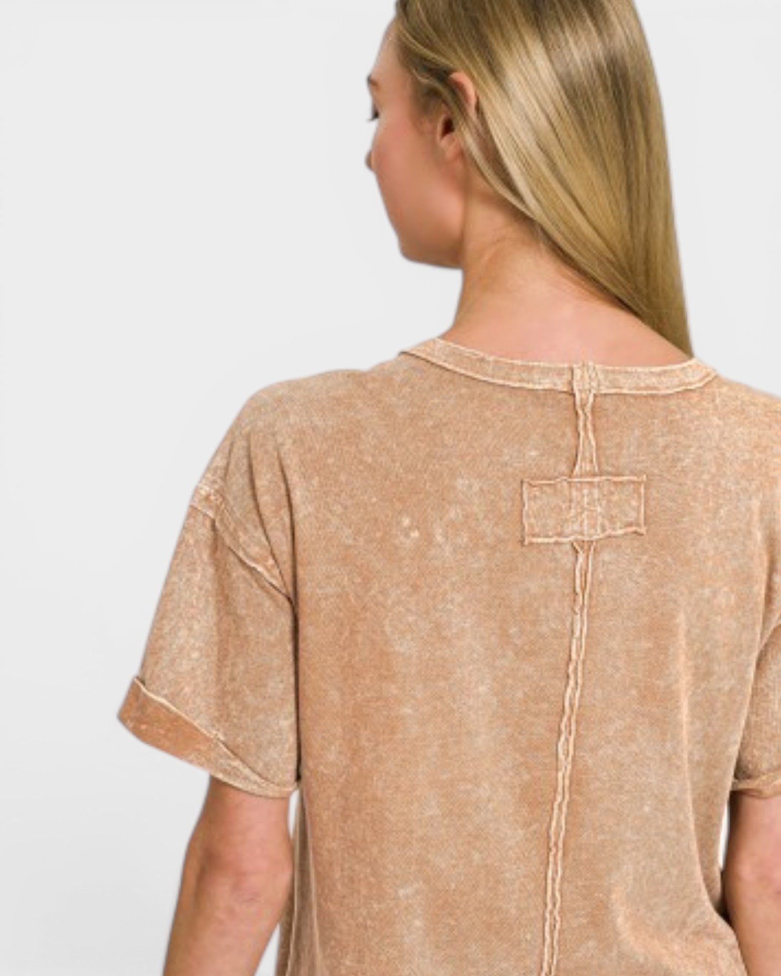 Woman wearing a beige t-shirt with a subtle pattern on a plain background