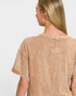 Woman wearing a beige t-shirt with a subtle pattern on a plain background