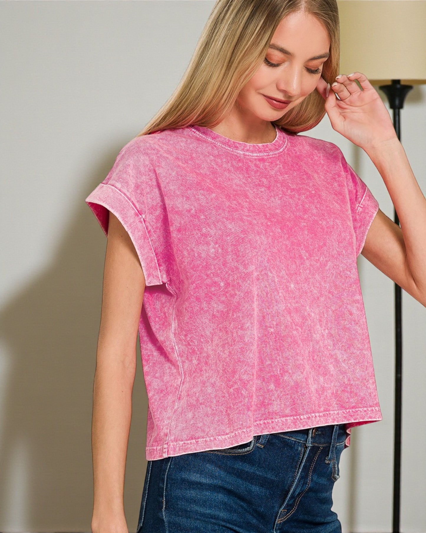 Woman wearing a pink acid-wash t-shirt and blue jeans indoors.