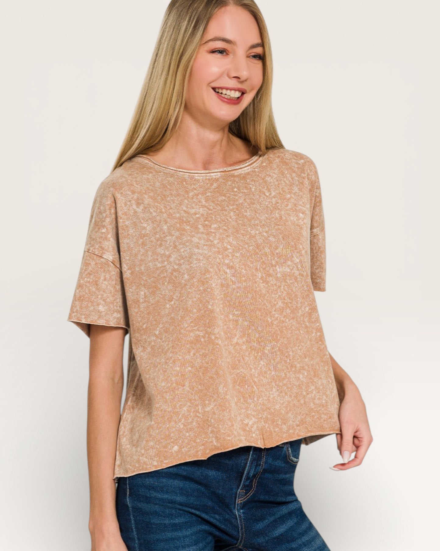 Woman wearing a beige marled top and blue jeans on a white background