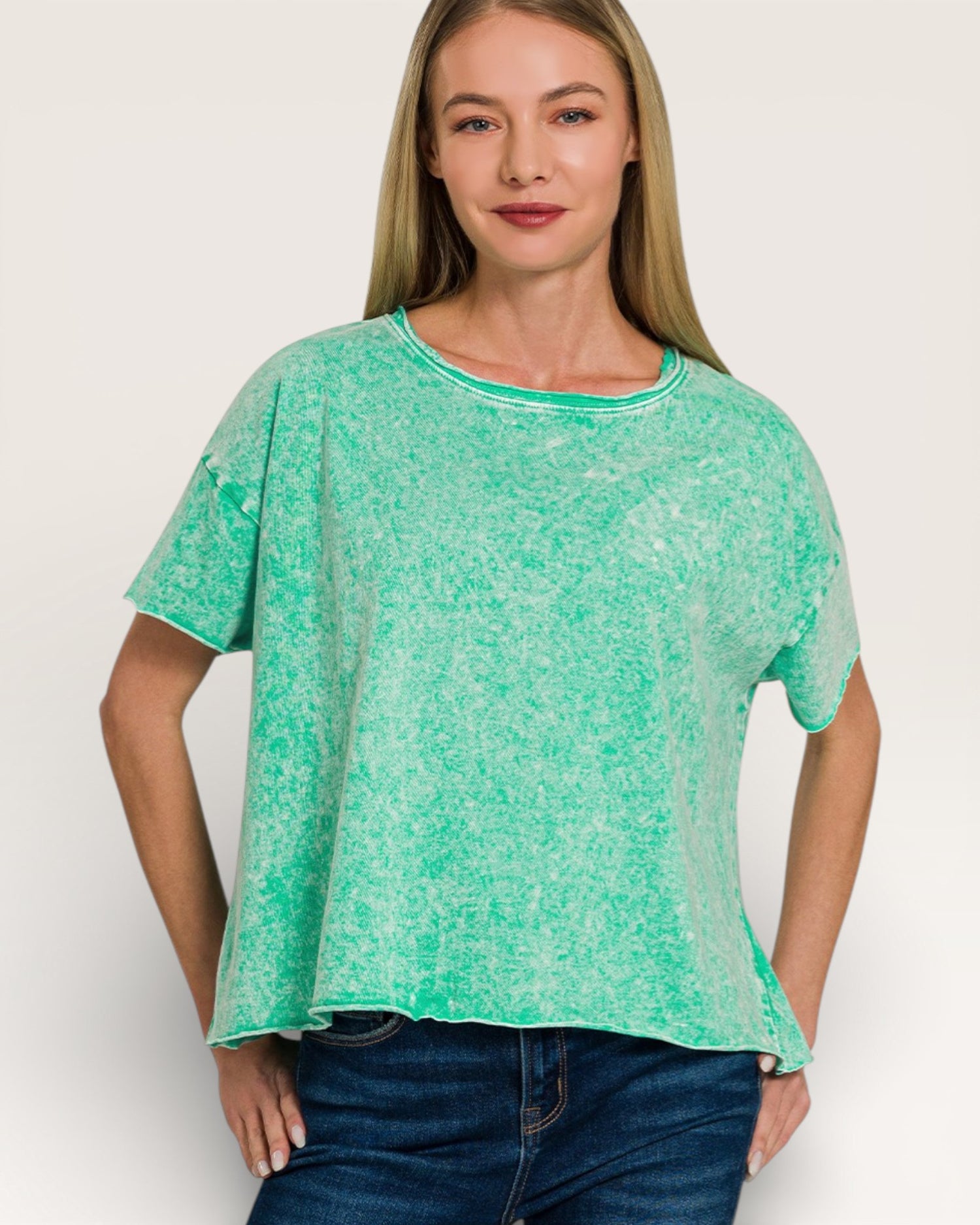 Woman wearing a green patterned top and blue jeans on a white background