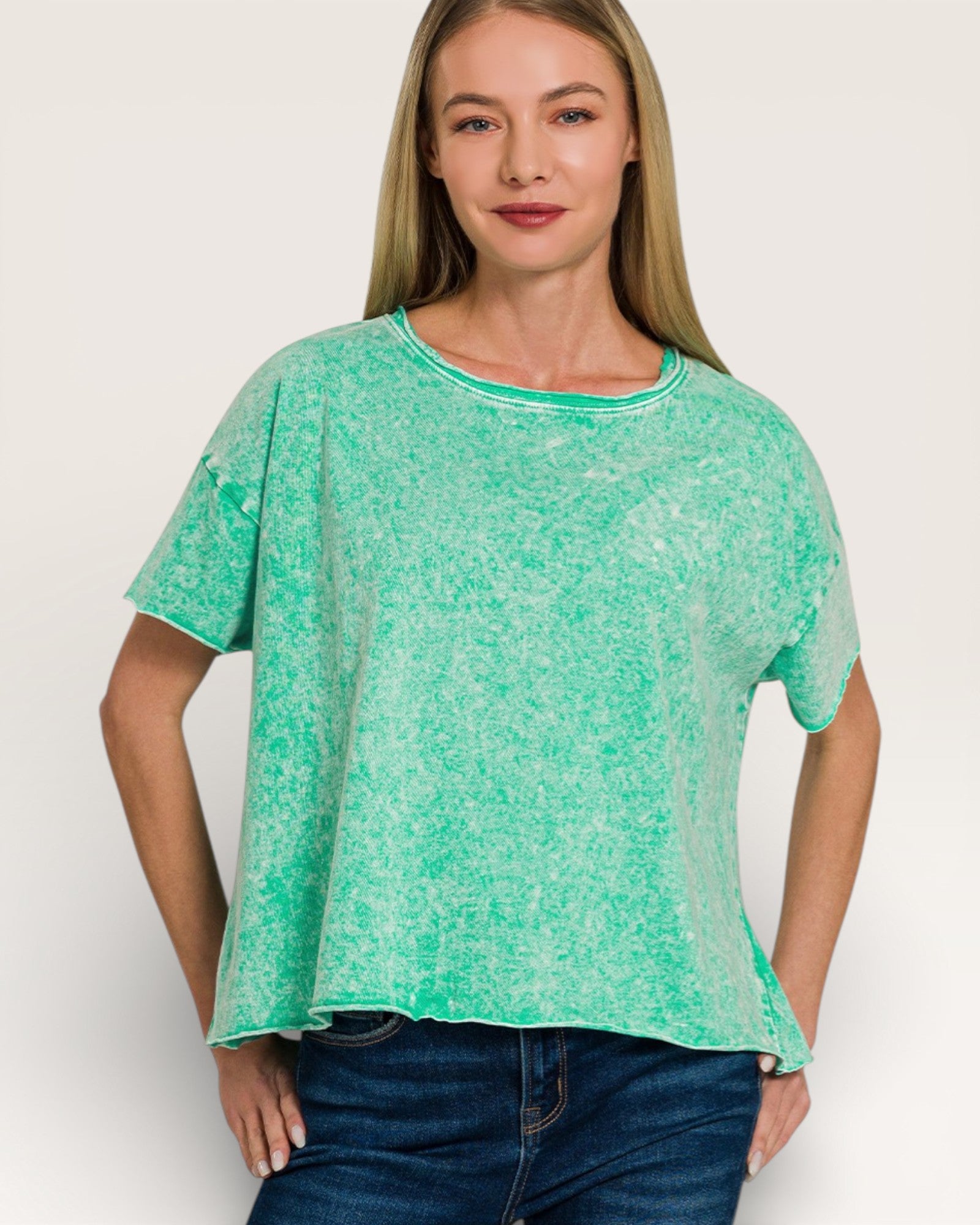 Woman wearing a green patterned top and blue jeans on a white background