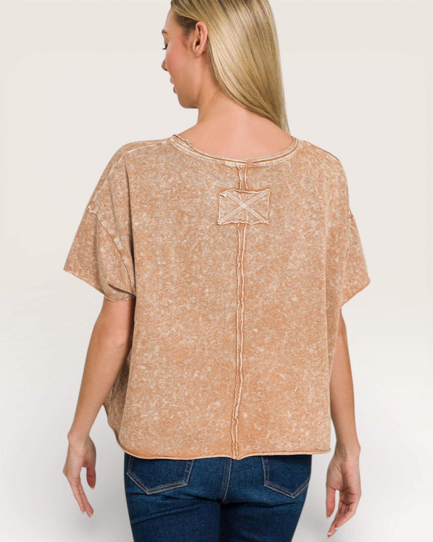 Woman wearing a beige patterned top with a decorative back detail on a plain background