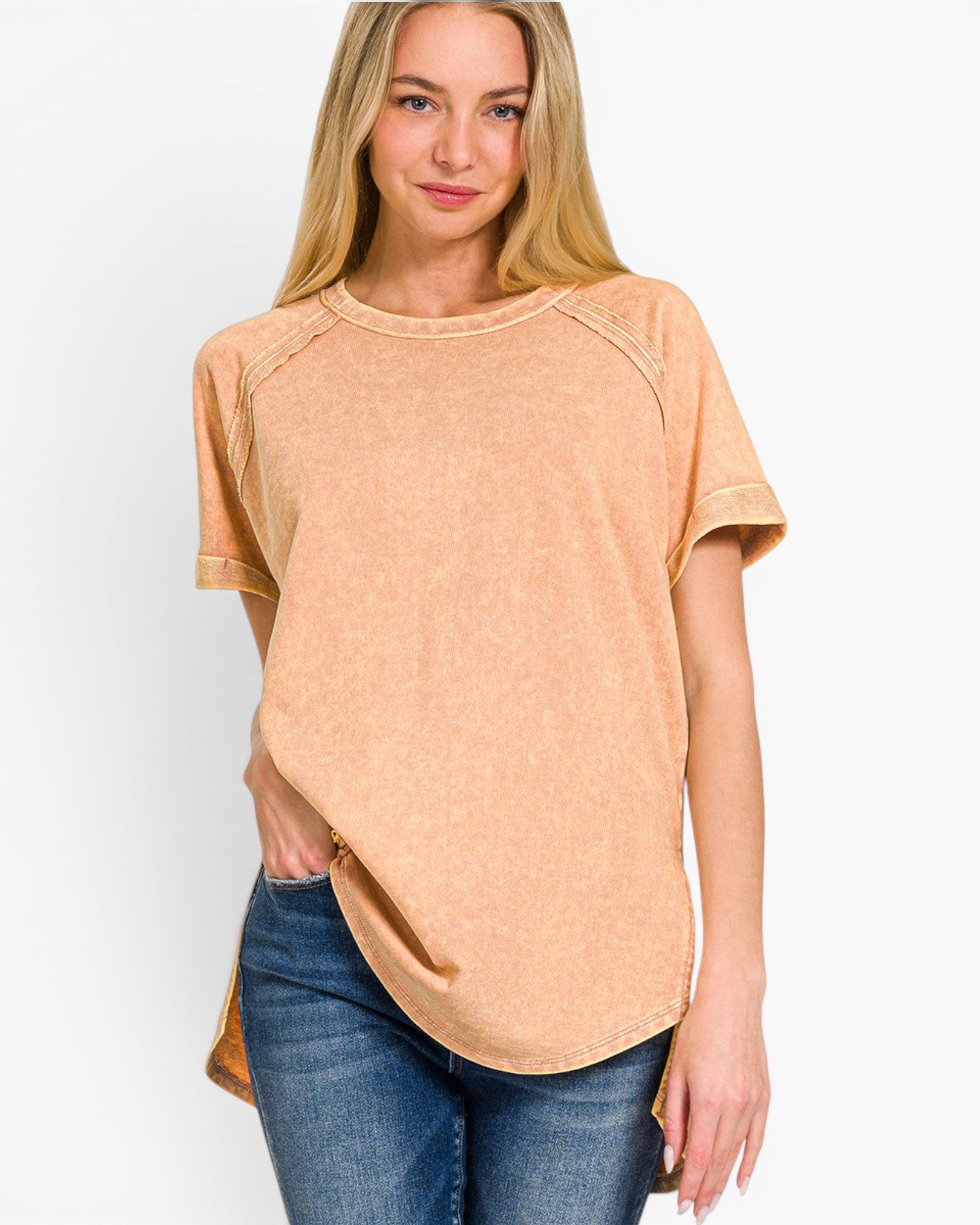 A woman wearing a short-sleeve, crew-neck t-shirt in a washed peach-beige color, paired with blue jeans, against a plain white background.