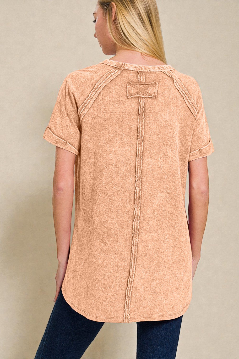 Woman wearing a peach-colored short-sleeve top with buttons on a beige background